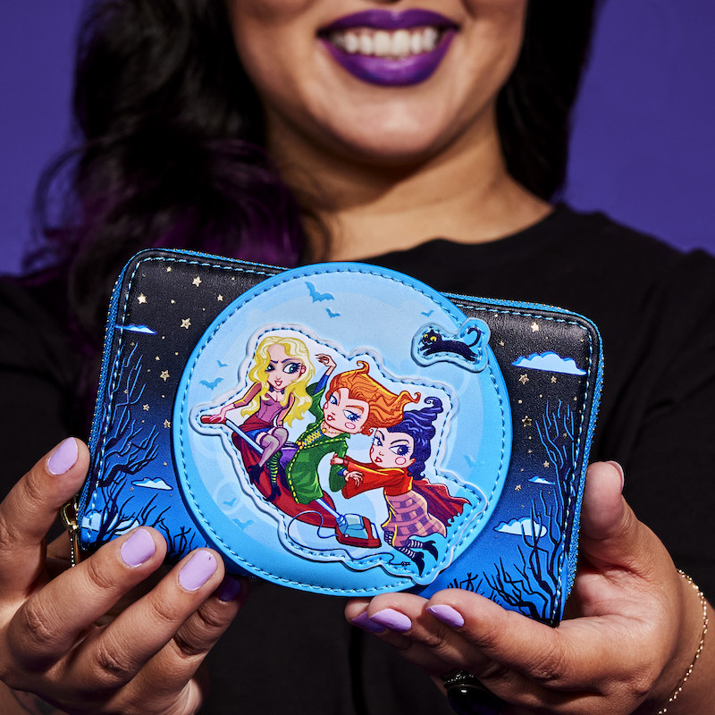 Woman holding the Hocus Pocus Poster Glow Zip Around Wallet toward camera, featuring the Sanderson sisters riding on a vacuum against the full moon.